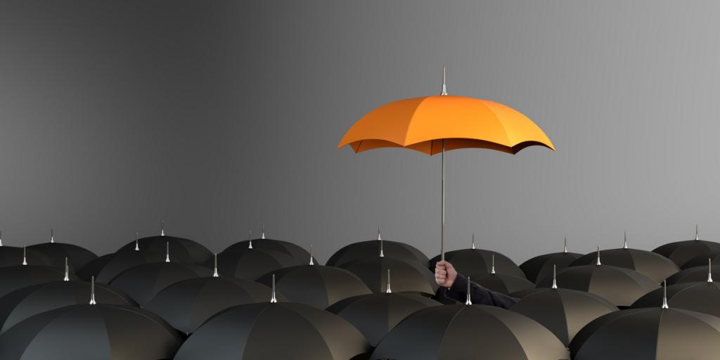 Orange umbrella above a large number of dark umbrellas - Copyright iStock-918117162